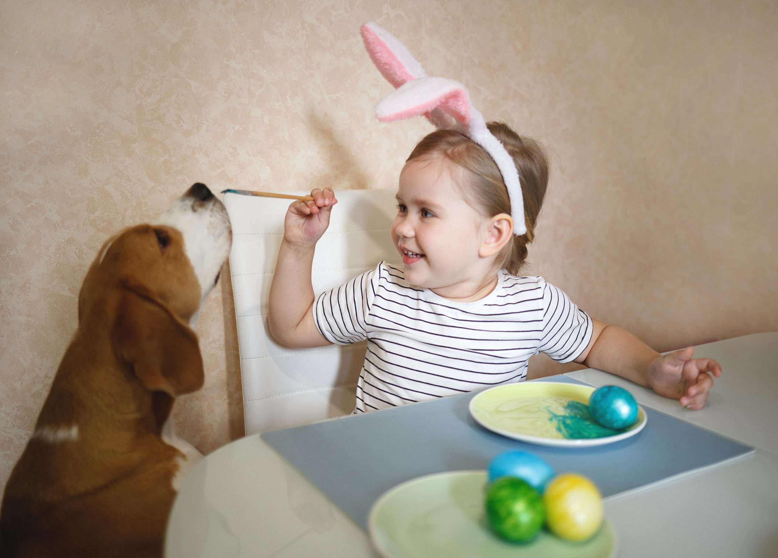 Kind mit Hasenohren malt Ostereier mit Hund.