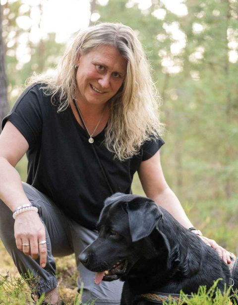 Frau und schwarzer Hund im Wald